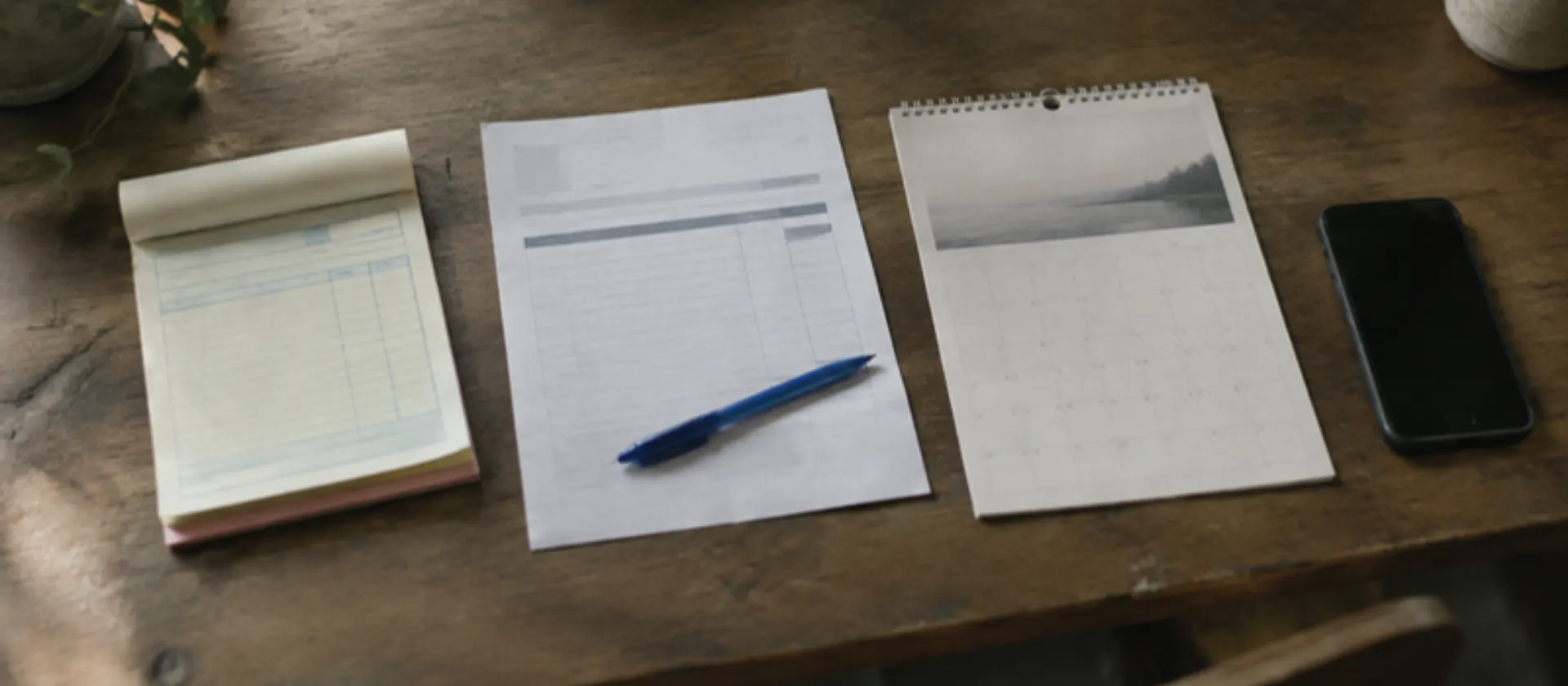 A quote pad, an invoice, a calendar page and a phone laid out on a desk